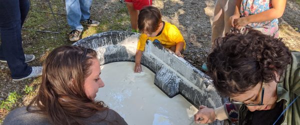 several adults and children sstanding near a bin of liquid