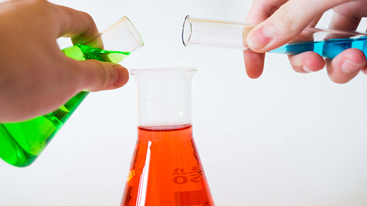 two people pouring beakers into another one