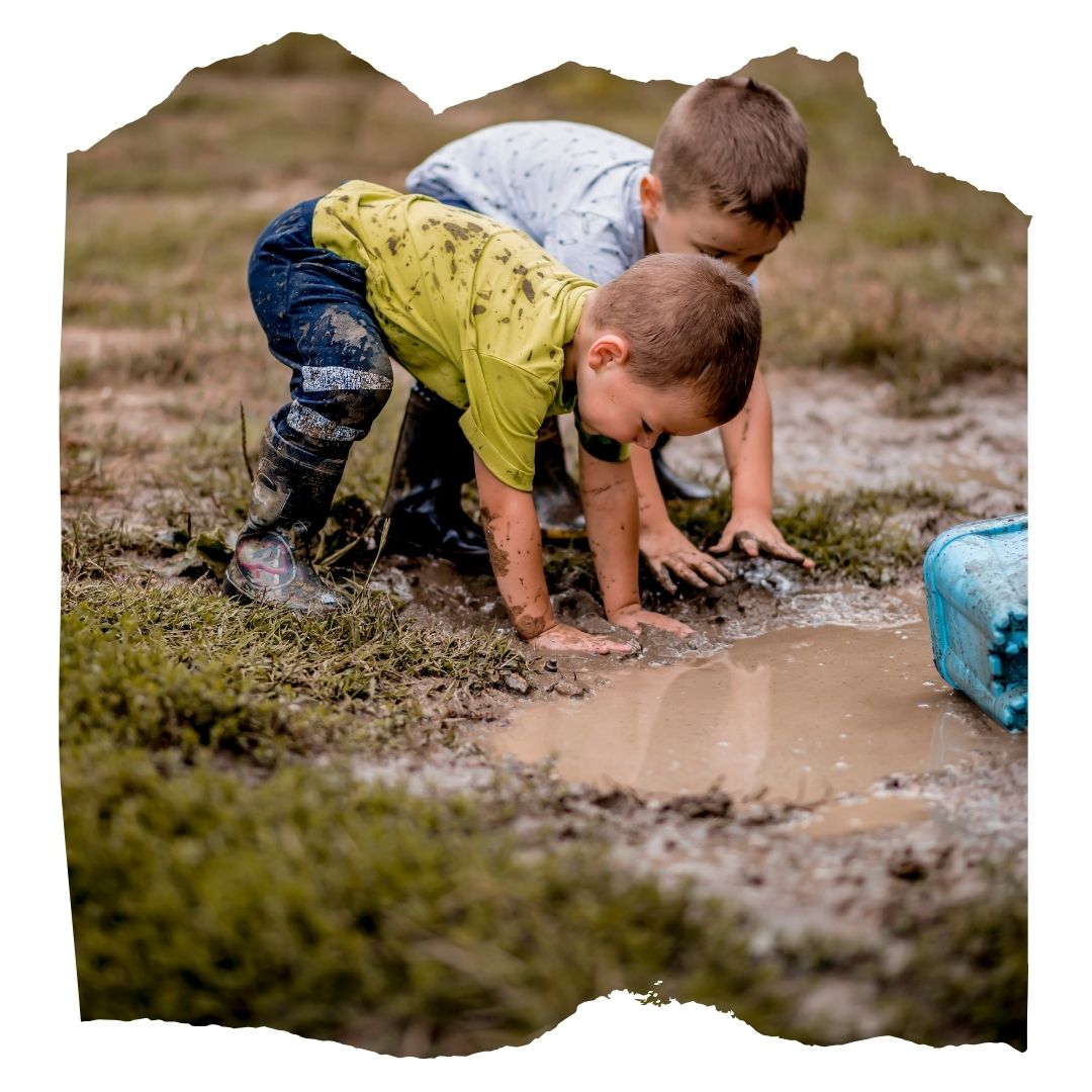 Two kids in rain boots playing in the mud